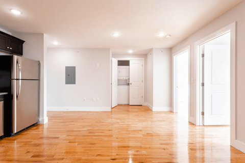 an empty living room with a wood floor and a refrigerator