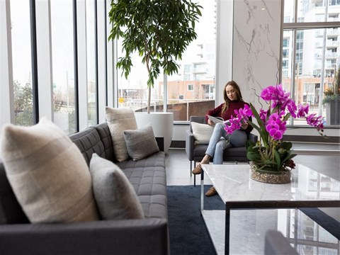 a woman sits on a couch in a living room with large windows