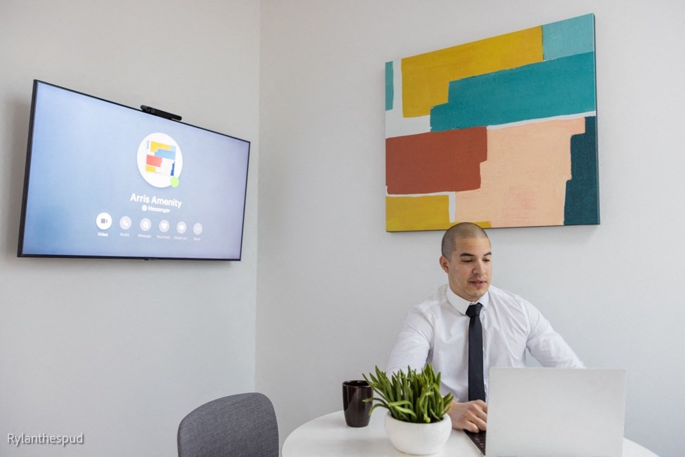 a man sitting at a desk with a laptop computer and a screen on the wall