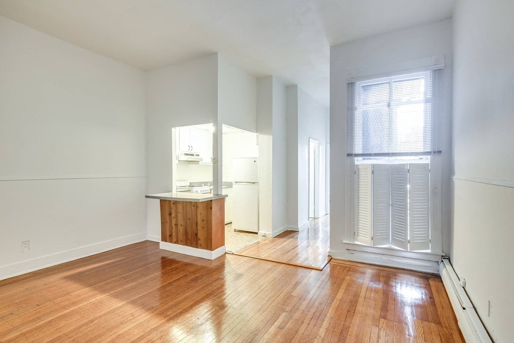 an empty living room with wood floors and a kitchen in the corner