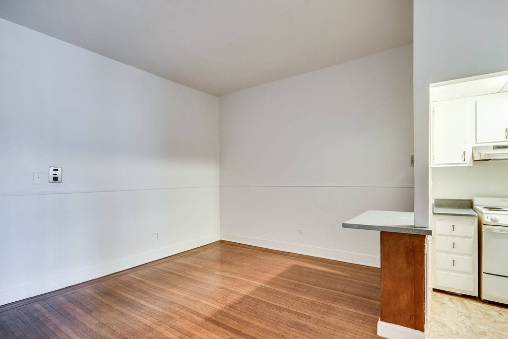 a living room with white walls and a kitchen with wood floors