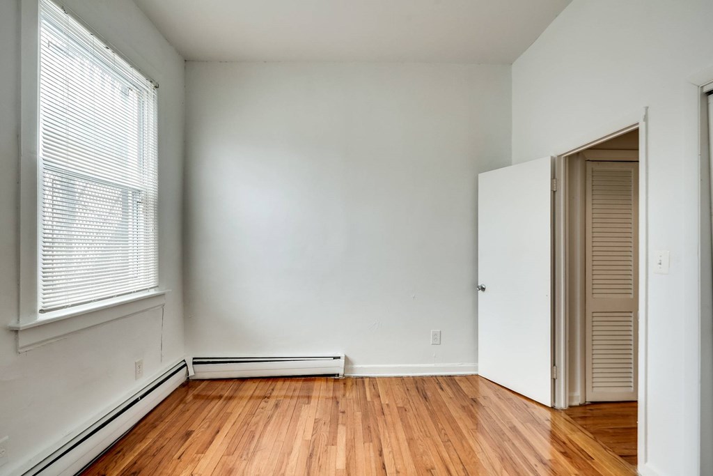 a bedroom with white walls and wood floors and a closet
