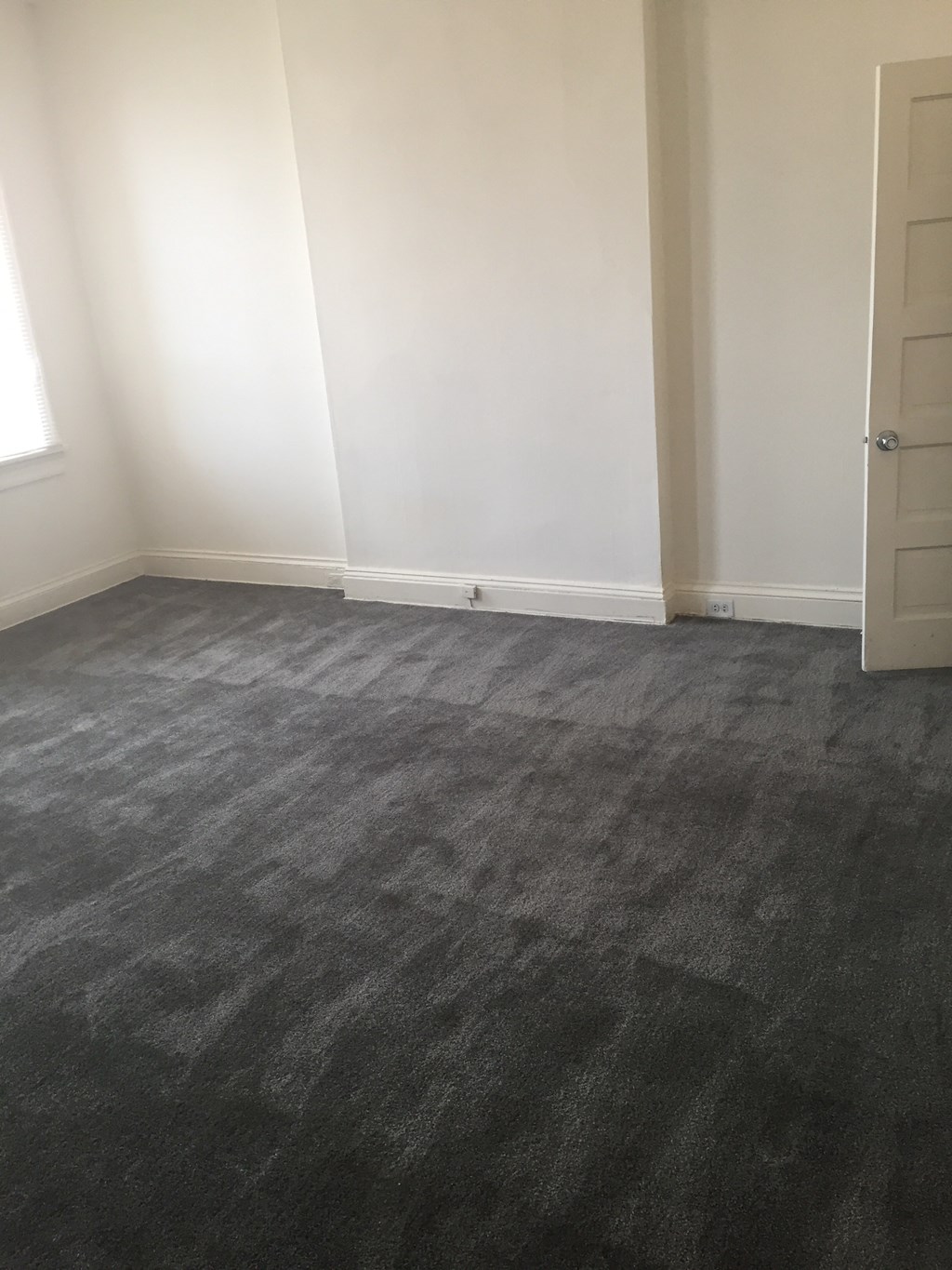 a room with a carpeted floor and white walls and a door