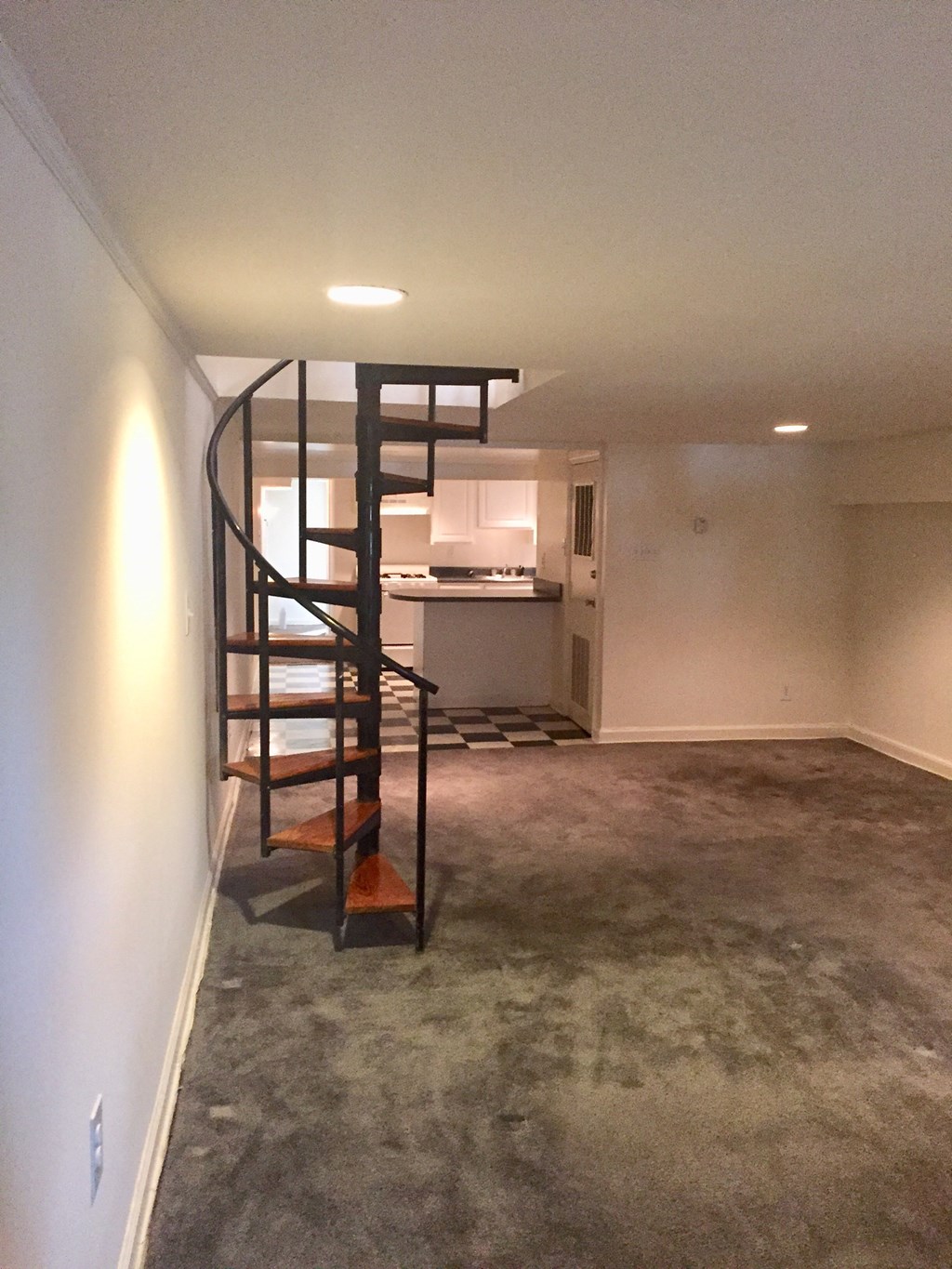 an empty living room with a spiral staircase and a kitchen