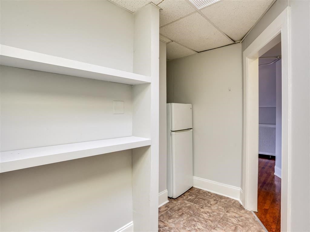 a walk in closet with white shelves and a refrigerator