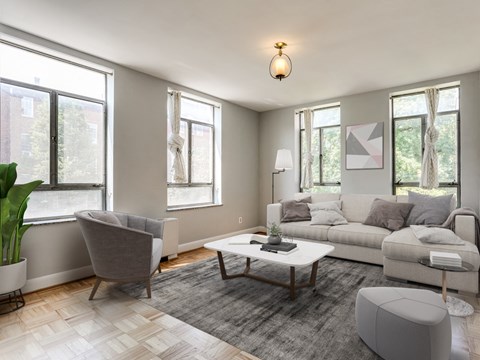 A modern living room with a grey sofa, a grey armchair, a wooden coffee table, and a grey ottoman.