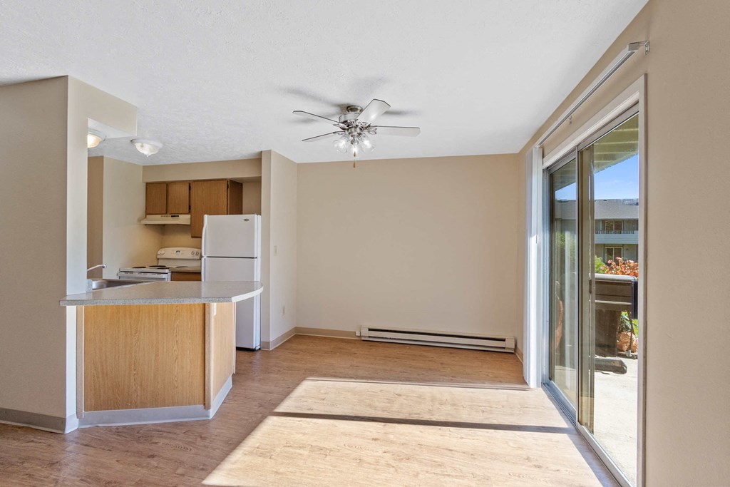 an empty living room with a kitchen and a ceiling fan