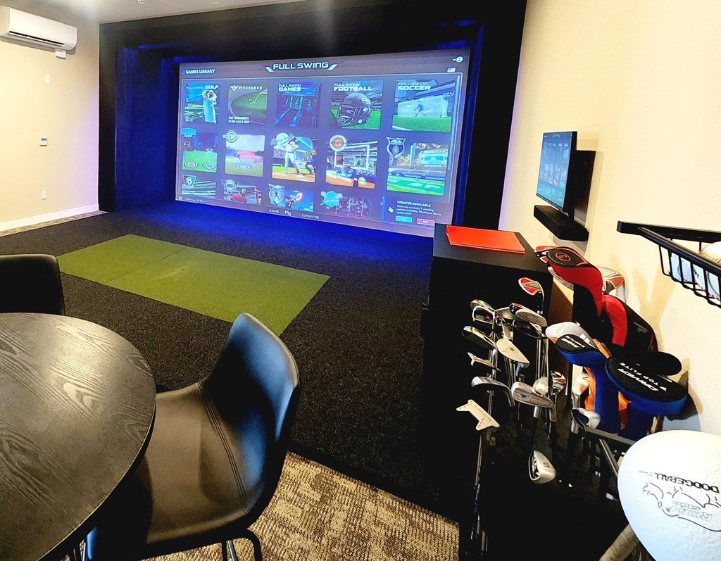 a gaming room with a large screen tv and a table with chairs made for golf simulator