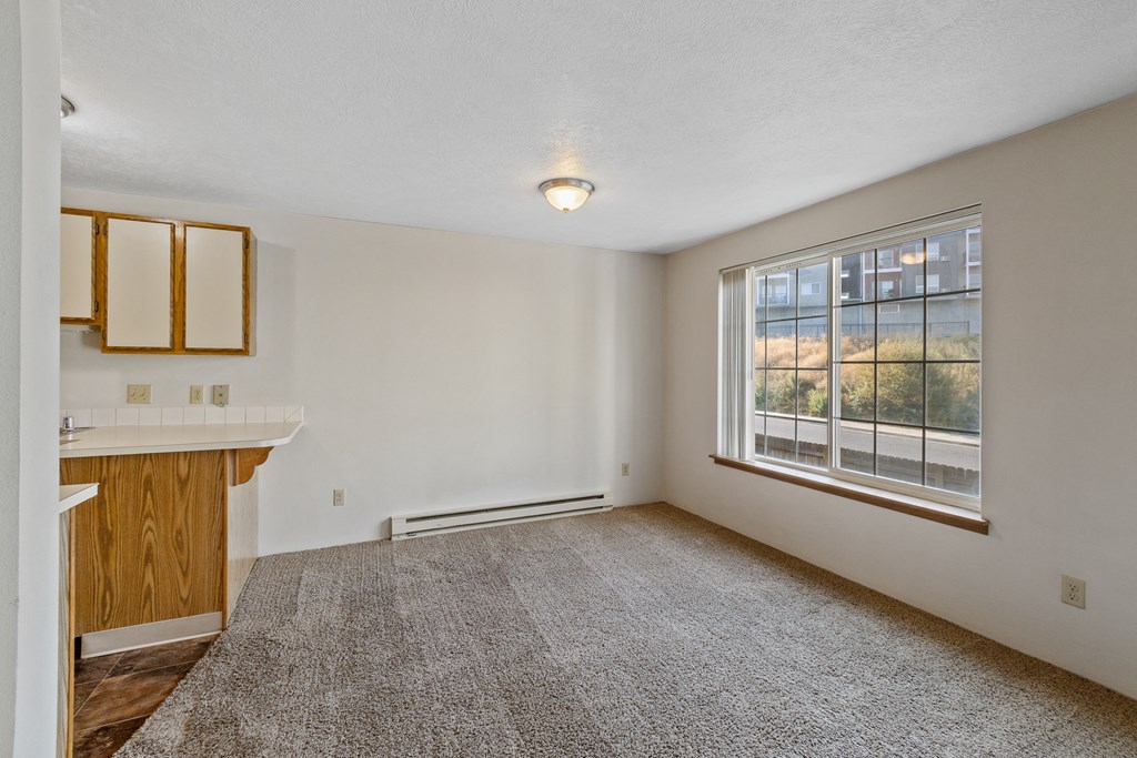 an empty living room with a large window and a kitchen