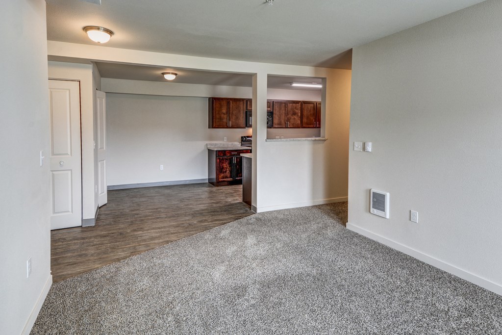 an empty living room with a kitchen in the background