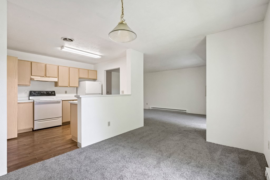 an empty living room and kitchen with white walls and wood flooring