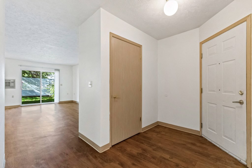 an empty living room with white walls and wooden floors and a door to a bedroom