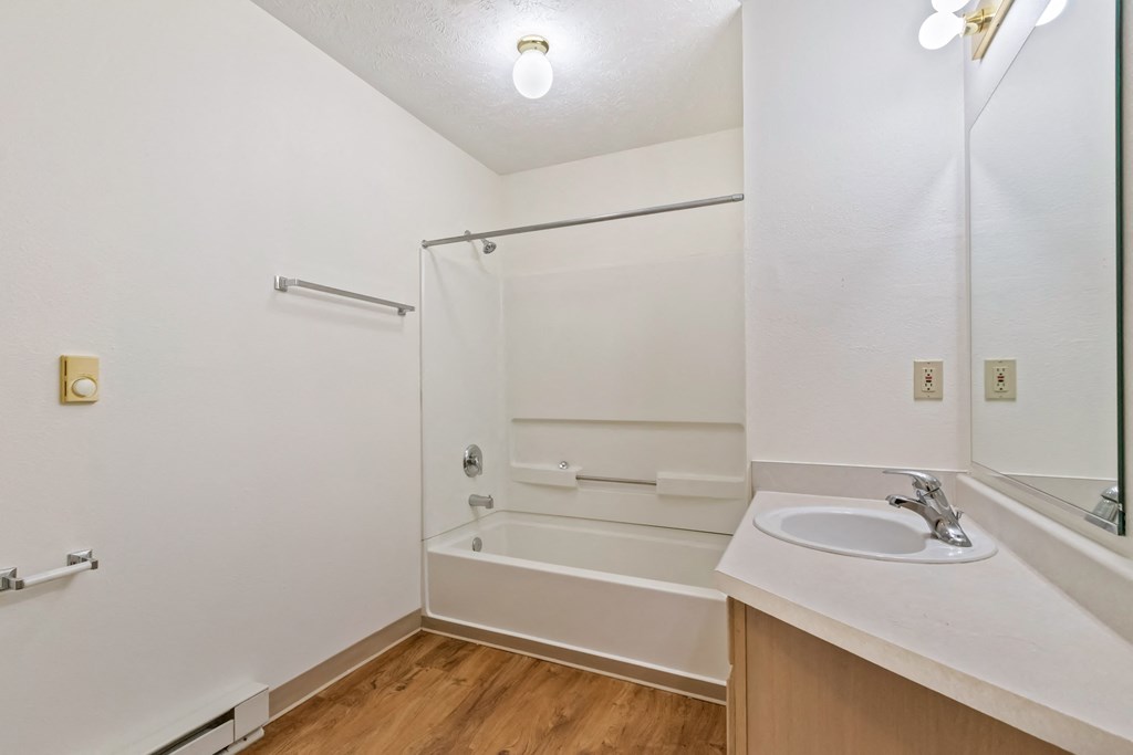 A white bathroom with a sink, mirror, and bathtub.