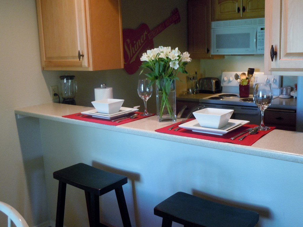 A kitchen with a table set for two with a vase of flowers on it.