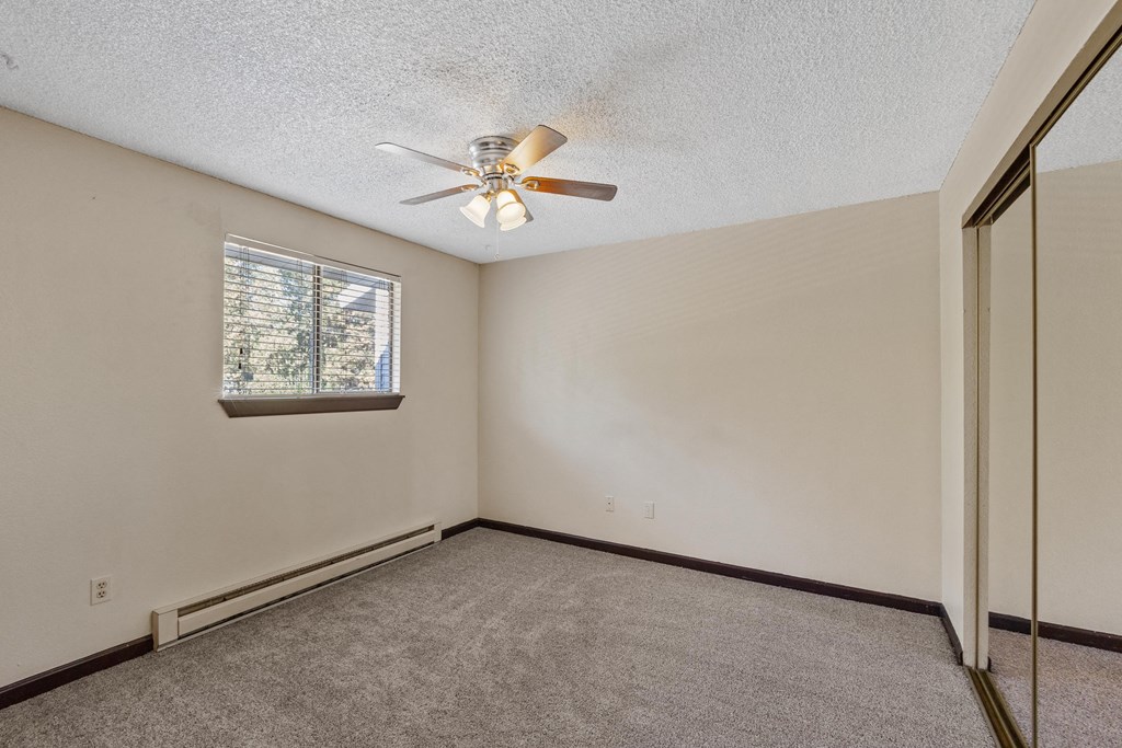 the living room of an empty home with a ceiling fan and a window