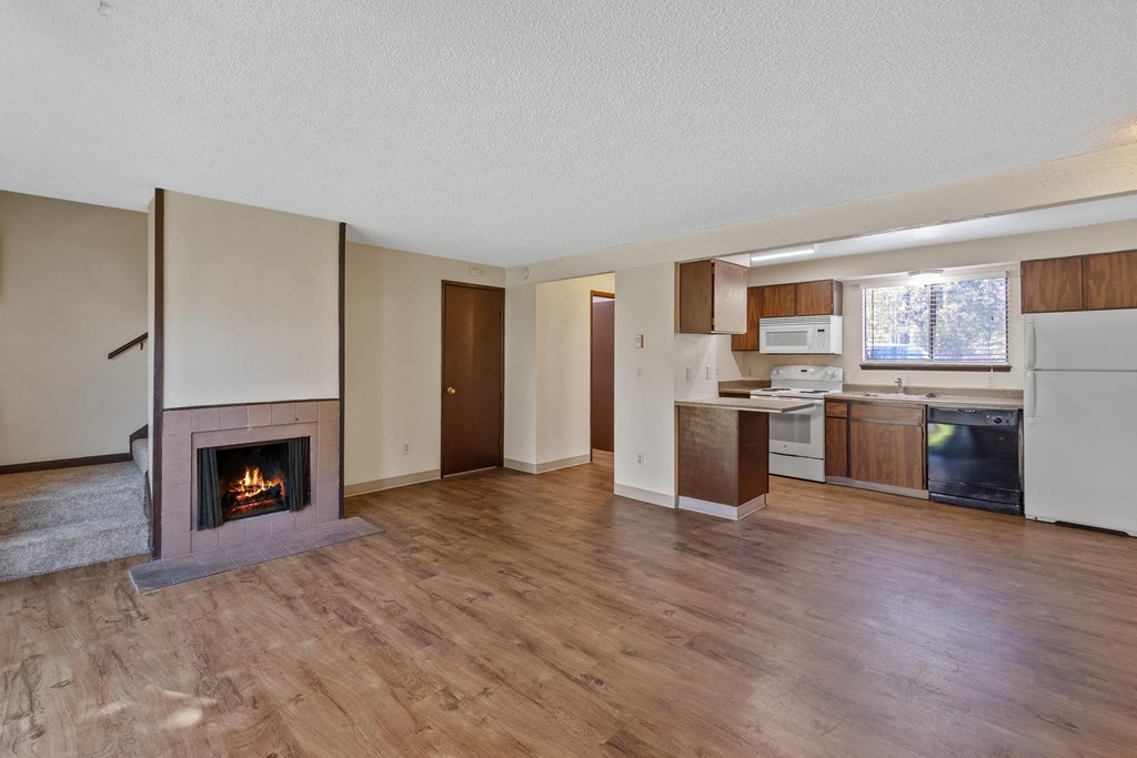 an empty living room with a fireplace and a kitchen