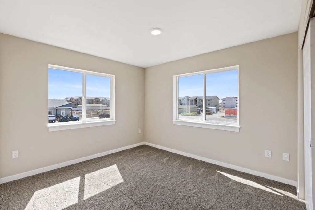 an empty bedroom with two windows and a carpeted floor