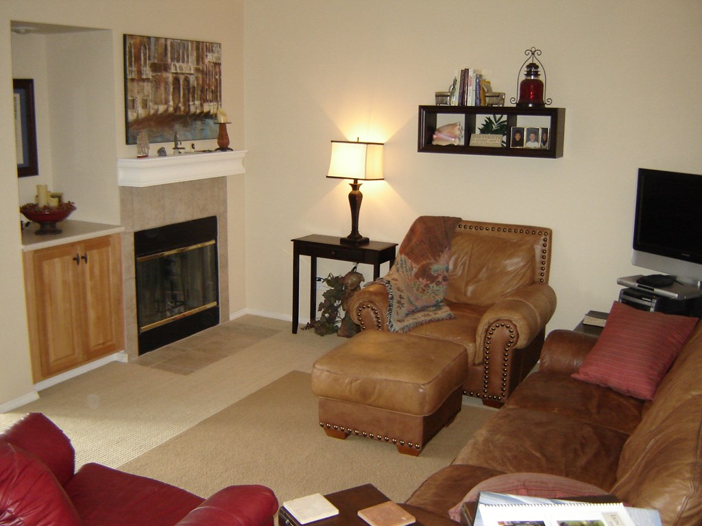 A living room with a fireplace, two chairs, a coffee table, and a painting on the wall.