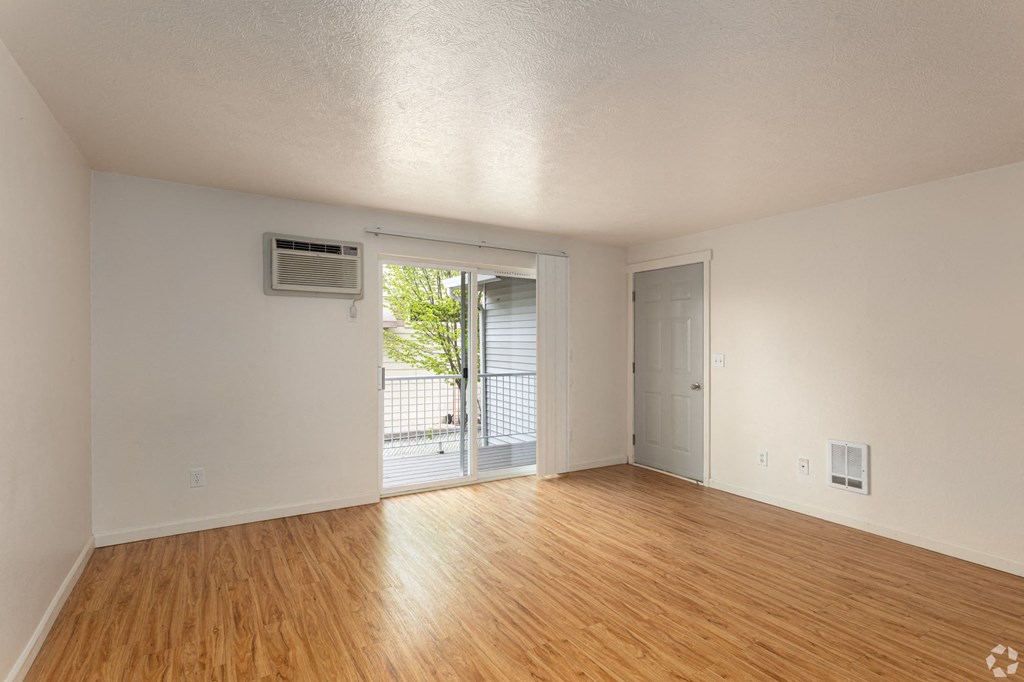 an empty living room with wood floors and a door to a balcony