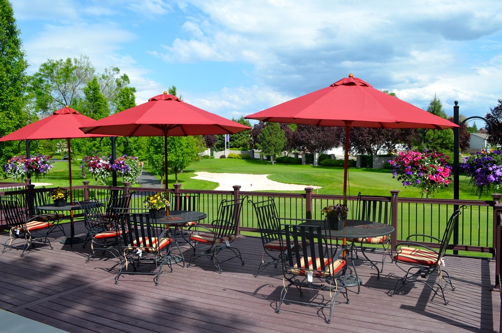 A patio with red umbrellas and chairs overlooking a green lawn.