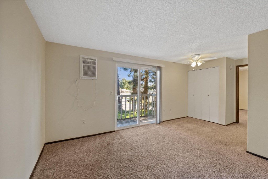 A room with a carpeted floor and a sliding glass door leading to a balcony.