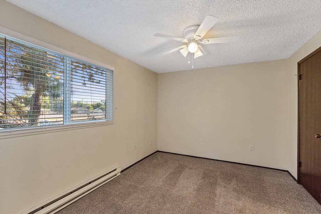 an empty living room with a large window and a ceiling fan