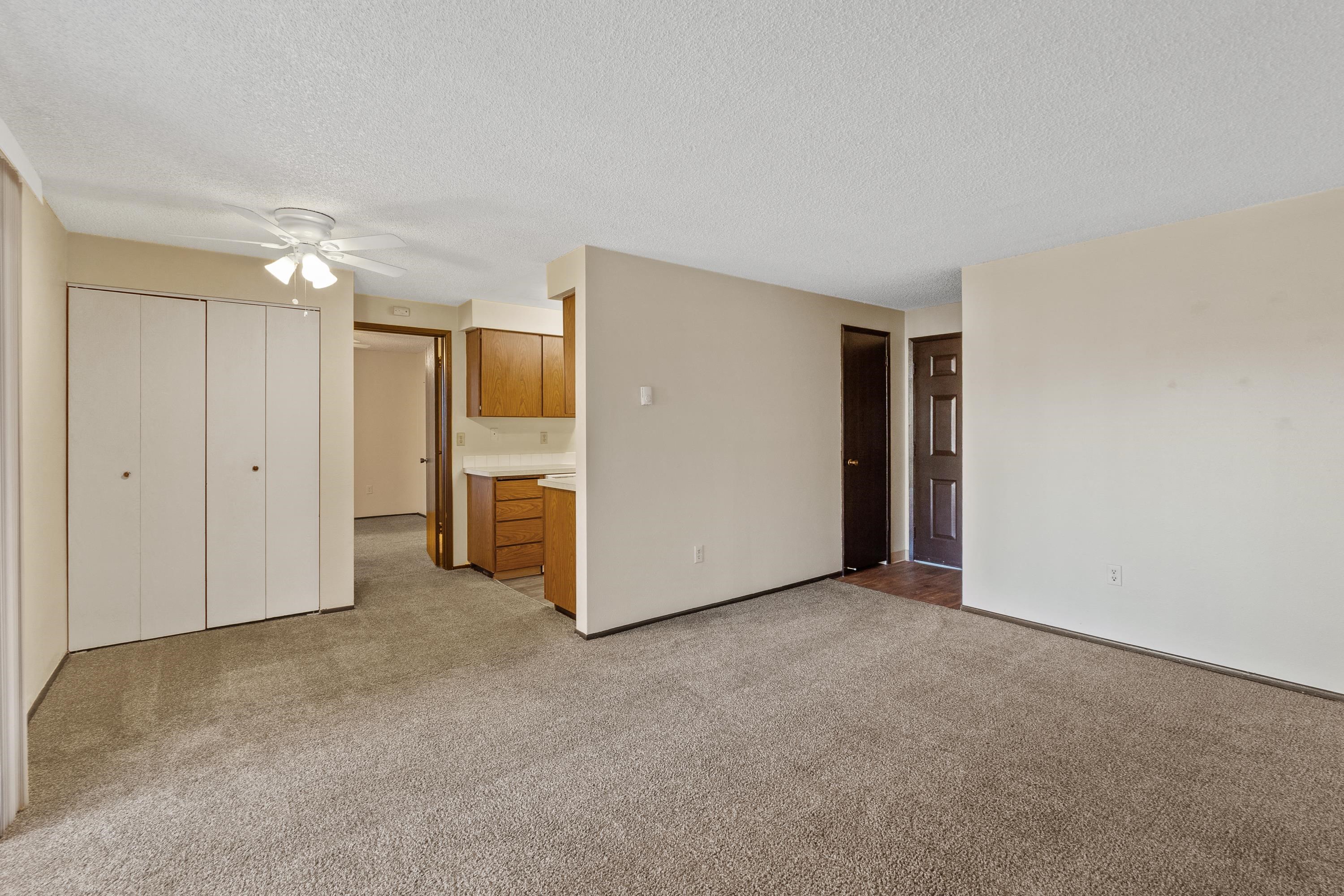 an empty living room with a kitchen and a ceiling fan