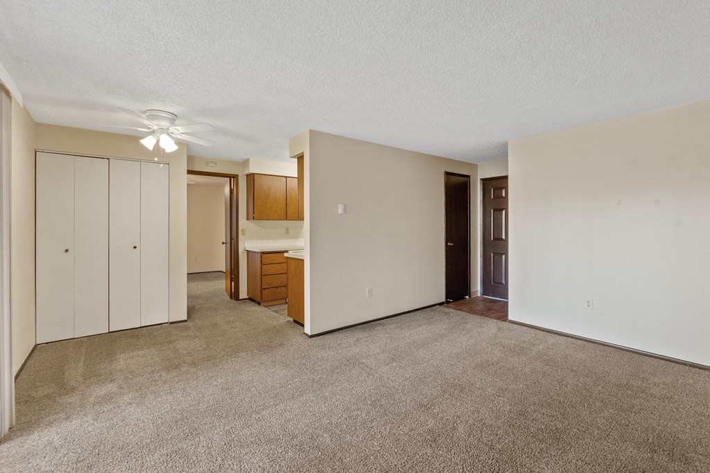 an empty living room with a kitchen and a ceiling fan