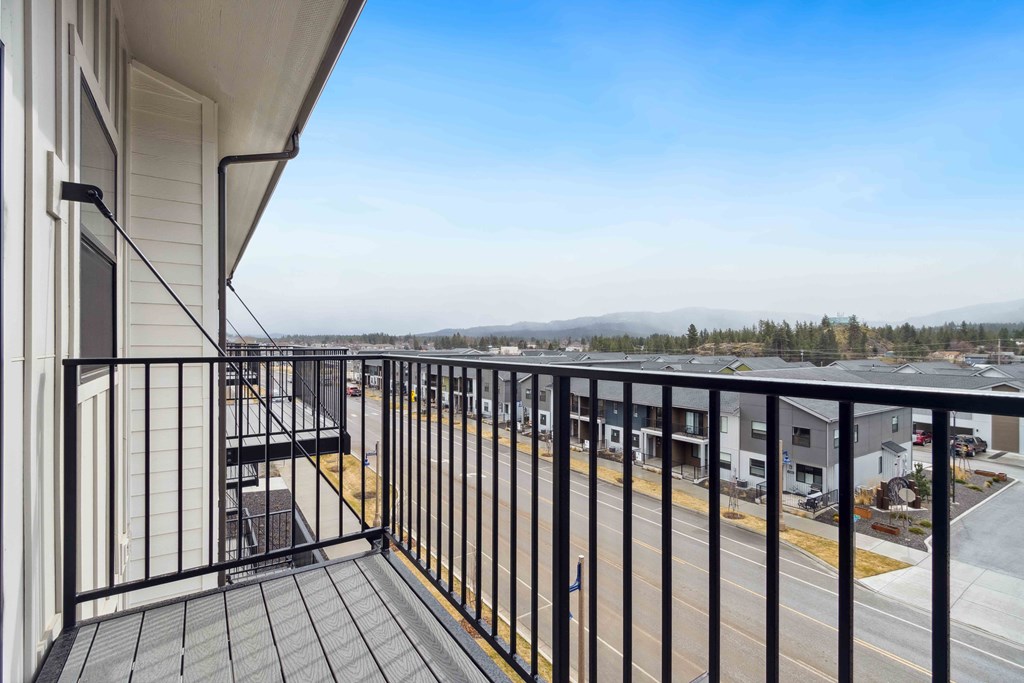 A balcony with a black railing and a view of a parking lot and distant trees.