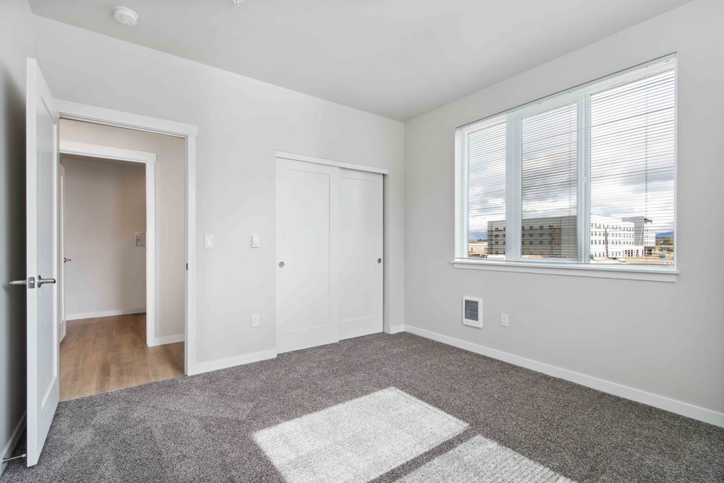 A room with a large rug in the middle and a window with blinds.