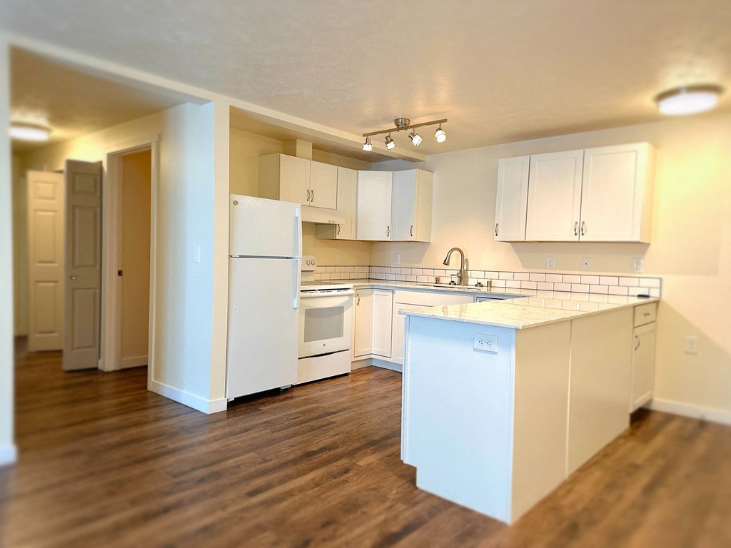 a large kitchen with white appliances and a wooden floor