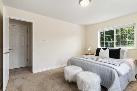 A bedroom with a bed, two stools, and a window.