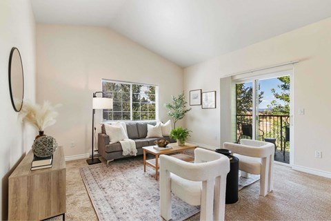A living room with a grey couch, a wooden coffee table, and a large window.