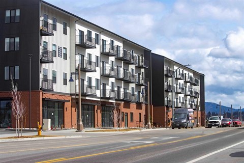 A modern apartment building with balconies and a parking lot in front.