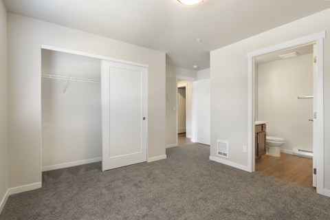 A sparsely furnished bedroom with a carpeted floor and white walls.