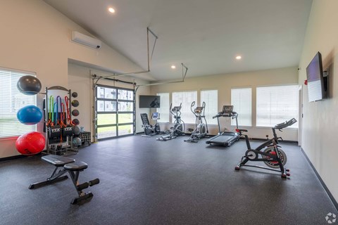 A spacious home gym with various exercise equipment and a television mounted on the wall.