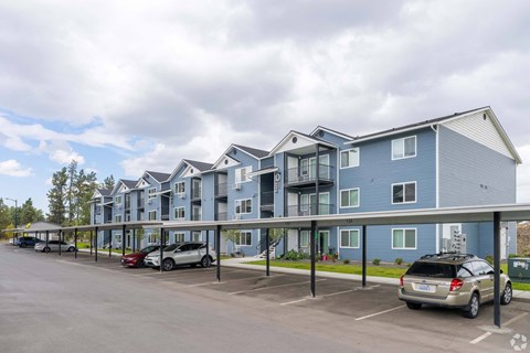A row of modern townhouses with cars parked in front.
