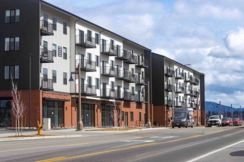 A modern apartment building with balconies and a parking lot in front.