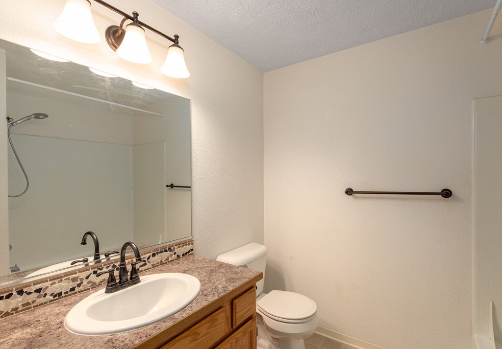 A bathroom with a sink, toilet, mirror, and light fixture.