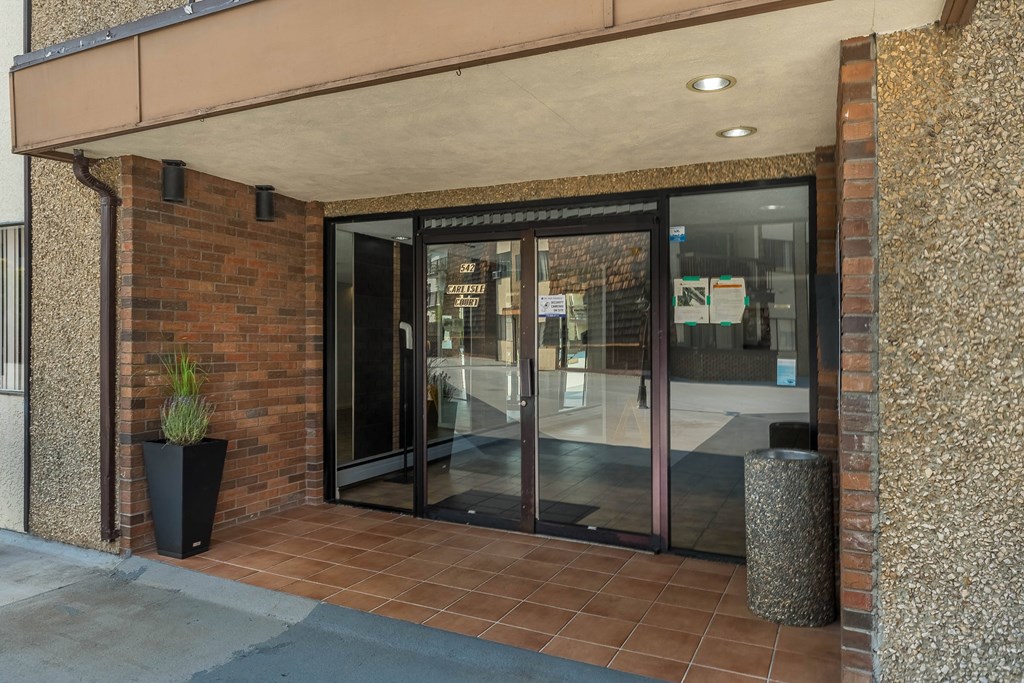 A glass door entrance to a building with a plant in a black pot to the left.