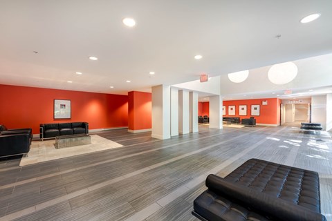 A spacious waiting area with black leather seating and orange walls.