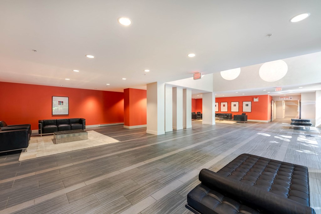 A spacious waiting area with black leather seating and orange walls.