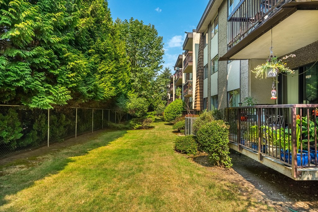 A balcony with a table and chairs overlooks a grassy area.