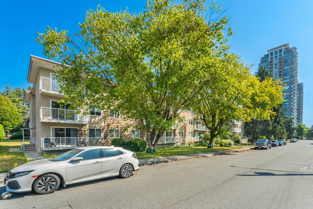 A white car is parked on the side of a street in front of a building with a tree in front of it.