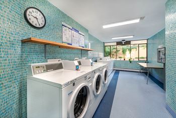 A laundromat with a washer and dryer, a clock, and a bench.
