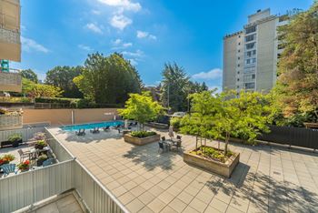 A rooftop patio with a pool, chairs, and trees.