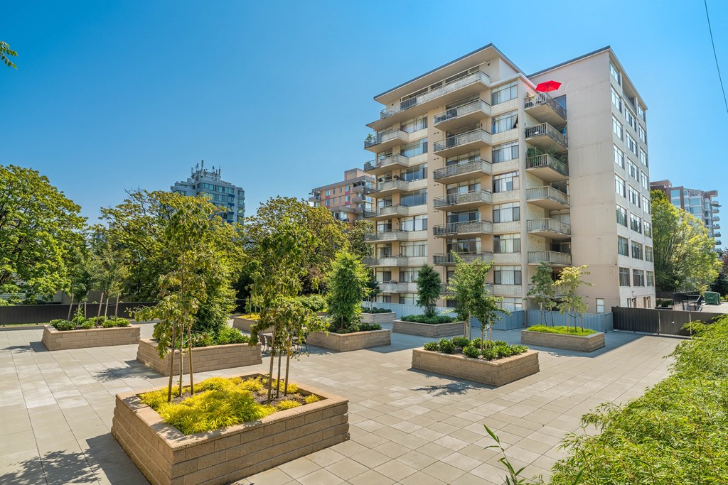 A modern apartment building with a courtyard garden in the foreground.
