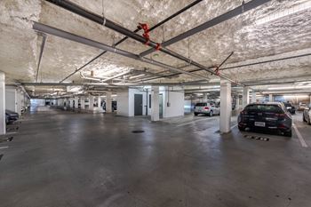 A parking garage with a concrete floor and a concrete ceiling with exposed pipes and ducts.