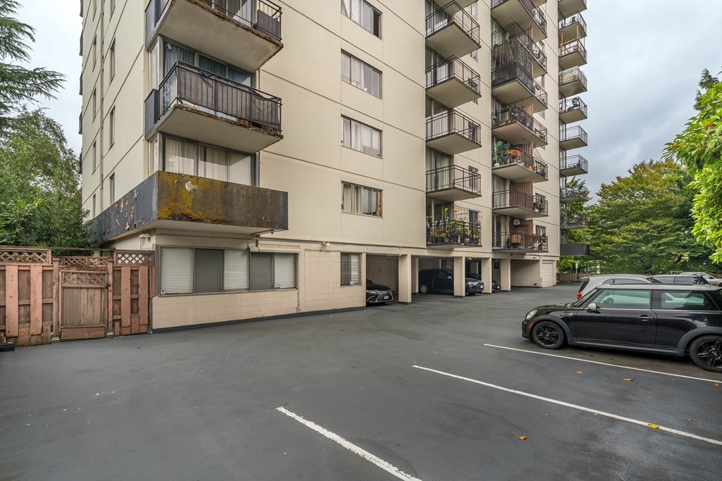 A black car is parked in a parking lot in front of a building.