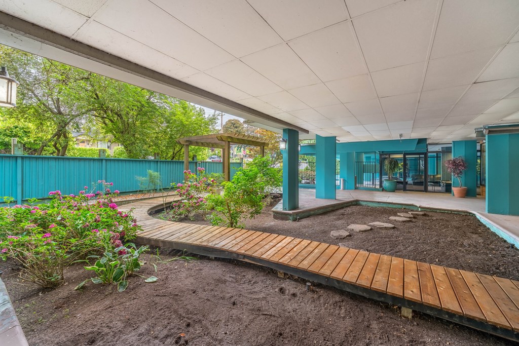 A garden with a wooden walkway and a green building in the background.